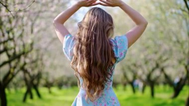 Mavi elbiseli esmer kadın Badem ağaçlarıyla dolu bir tarlada eğleniyor.