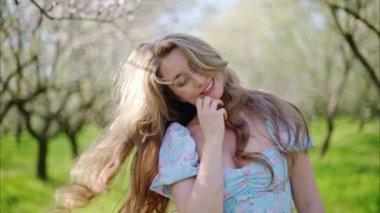 Mavi elbiseli esmer kadın çiçek açan badem ağaçlarının arasında dönüyor.