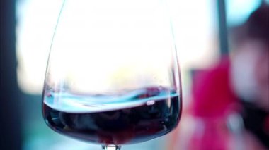 Kırmızı şarap, arka planda bulanık insanlar olan bir bardakta dönüp duruyor.