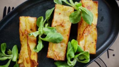 Kızarmış börek ve siyah tabakta kediotu salatası.