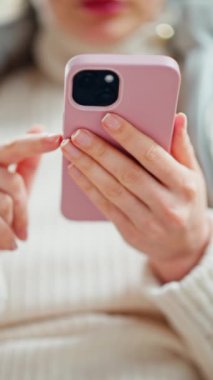Bir kafede ceketli bir kadın telefonunu karıştırıyor. Dikey