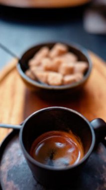 Tahta tepside kahverengi şeker küpleriyle siyah bir fincan espresso. Dikey