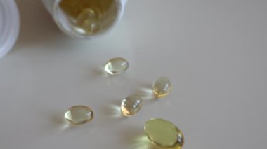 Balık yağı omega 3 takviyeleri beyaz arka planda bir paketleyiciden dökülüyor.