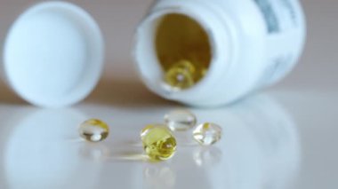 Balık yağı omega 3 takviyeleri beyaz arka planda bir paketleyiciden dökülüyor.