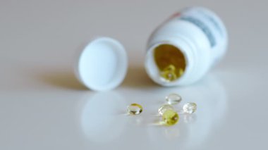 Balık yağı omega 3 takviyeleri beyaz arka planda bir paketleyiciden dökülüyor.