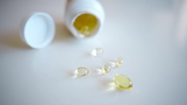 Balık yağı omega 3 takviyeleri beyaz arka planda bir paketleyiciden dökülüyor.