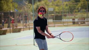 Siyah gömlekli bir adam güneşli bir günde mavi ve yeşil bir kortta tenis oynuyor.