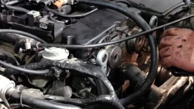 Kirli elleri olan bir adam bir arabanın motor bölmesinde çalışıyor.