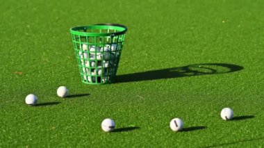 Güneşli bir günde golf toplarıyla dolu yeşil bir kova.