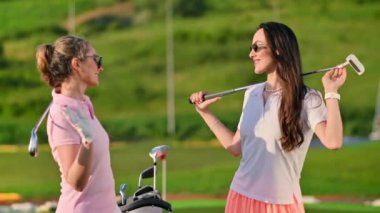 İki kadın omuzlarında golf sopalarıyla güneşli bir günde beşlik çakıyor.