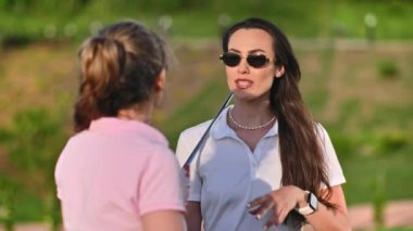 Güneşli bir günde golf sahasında konuşan iki kadın.