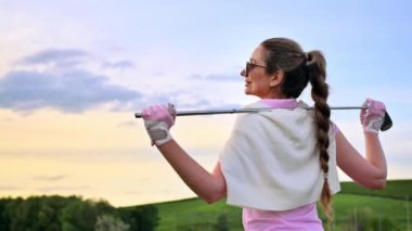 Omuzlarında golf sopası tutan bir kadın gün batımını seyrediyor.