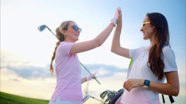 Güneşli bir günde golf sopası tutan ve beşlik çakan iki kadın.