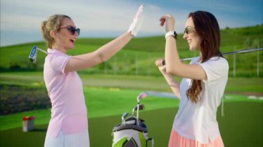 İki kadın omuzlarında golf sopalarıyla güneşli bir günde beşlik çakıyor.