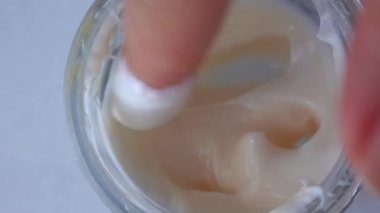Kadın parmağı kavanozdan krema topluyor.