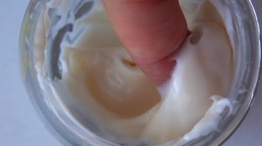 Kadın parmağı kavanozdan krema topluyor.