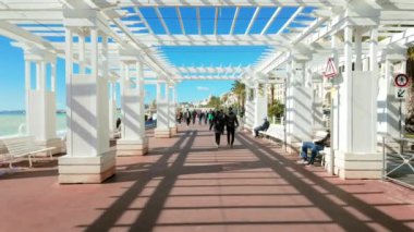 Güzel, Fransa - 7 Temmuz 2024: İnsanlar sahildeki Promenade des Anglais 'de beyaz yolda yürüyorlar
