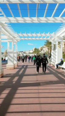Nice, Fransa - 7 Temmuz 2024: İnsanlar sahildeki Promenade des Anglais 'de beyaz geçitte yürüyorlar. Dikey