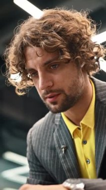 Sarı gömlekli ve gri ceketli bir adam kablosuz kulaklıklarıyla konuşuyor. Dikey