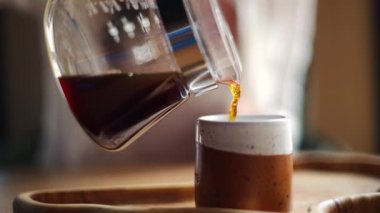 Tahta bir tepside duran bir bardağa kahve dolduran bir kadının yakın plan fotoğrafı.