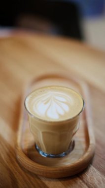 Kafedeki bir masada, ahşap tepside duran bir bardak latte. Dikey