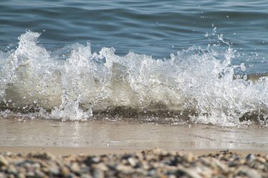 Beyaz köpük ve deniz suyu, kum ve mavi suyla ağır çekimde sıçrar.