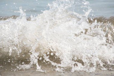 Beyaz köpük ve deniz suyu, kum ve mavi suyla ağır çekimde sıçrar.