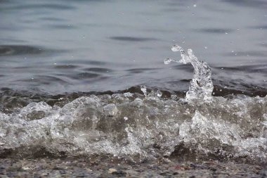 Beyaz köpük ve deniz suyu, kum ve mavi suyla ağır çekimde sıçrar.