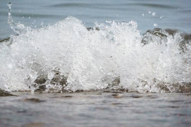 Beyaz köpük ve deniz suyu, kum ve mavi suyla ağır çekimde sıçrar.