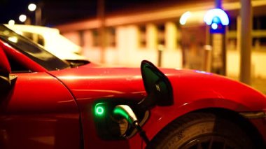 Gece sokakta kırmızı, elektrikli araba şarj oluyor.