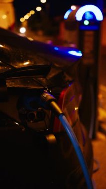 Siyah, elektrikli araba gece sokakta şarj oluyor. Dikey
