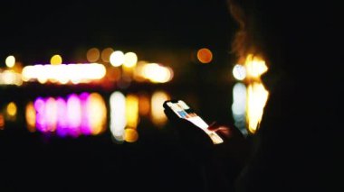Geceleri sahilde telefonunu kaydıran bir kadın.