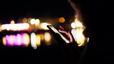 Geceleri sahilde telefonunu kaydıran bir kadın.