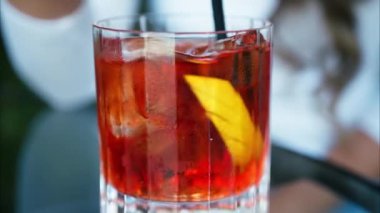 Negroni kokteylini pipetle karıştıran bir kadının yakın çekimi.