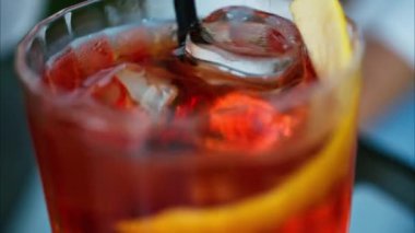 Negroni kokteylini pipetle karıştıran bir kadının yakın çekimi.