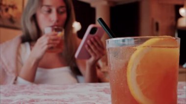 Bir restoranın arka planında bir kadın olan portakal kokteylini masaya yakın.