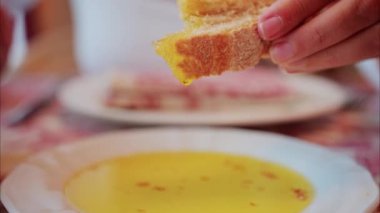 Bir kadının bir parça ekmeğini yağ tabaklarına bandırması.