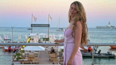 Cannes, Fransa 'da akşam vakti plajda pembe elbiseli bir kadın poz veriyor.