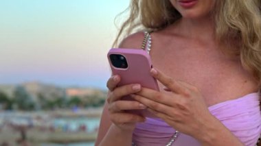 Pembe elbiseli kadın Cannes, Fransa 'da akşam kumsalda telefonuyla kayıyor.
