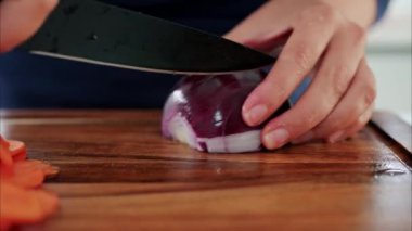 Tahta kesme tahtasıyla diğer sebzelerin yanında kırmızı soğan doğrayan bir kadının fotoğrafını çek.