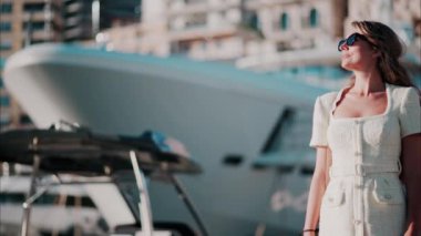 Beyaz elbiseli esmer kadın. Arka planda bulanık bir liman manzarası var.