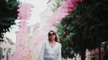 Fransa 'nın Grasse kentinin caddelerinde pembe şemsiye sıralarının altında yürüyen bir kadın.