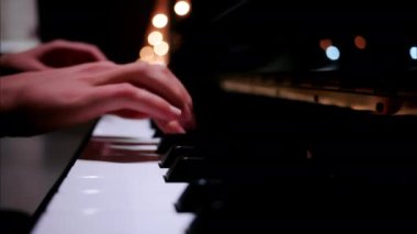 Arka planda bulanık ışıklarla piyano çalan bir kadının ellerini kapatın.