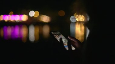 Geceleri sahilde telefonundaki resimlere bakan bir kadın.