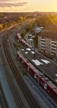 Danimarka 'nın Kopenhag bölgesindeki Vesterbro bölgesinde gün batımında hareket eden bir trenin insansız hava aracı görüntüsü. Dikey