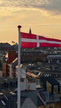 Gün batımında Kopenhag 'daki bir binanın tepesinde sallanan Danimarka bayrağının insansız hava aracı görüntüsü. Dikey