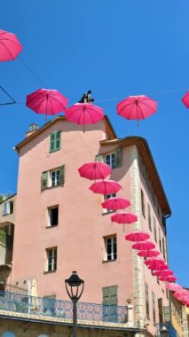 Grasse, Fransa 'daki eski kasabanın sokaklarının üzerinde arka planda bir bina bulunan pembe şemsiye sıraları. Dikey