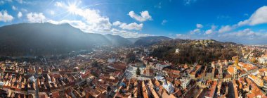 Brasov şehrinin sonbahar mevsiminde eski merkezinin hava aracı görüntüsü. Dağlar ve bulutlu mavi gökyüzü. Romanya