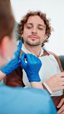 Diş hekimi koruyucu maske takıyor, gözlük takıyor ve dişçi dolabındaki bir hastanın dişlerini kontrol ediyor. Dikey