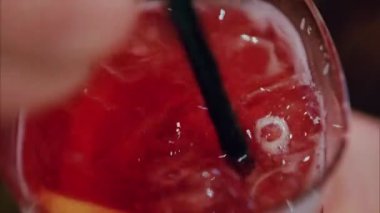 Kırmızı kokteyli siyah pipetle karıştıran bir kadının yakın çekimi.